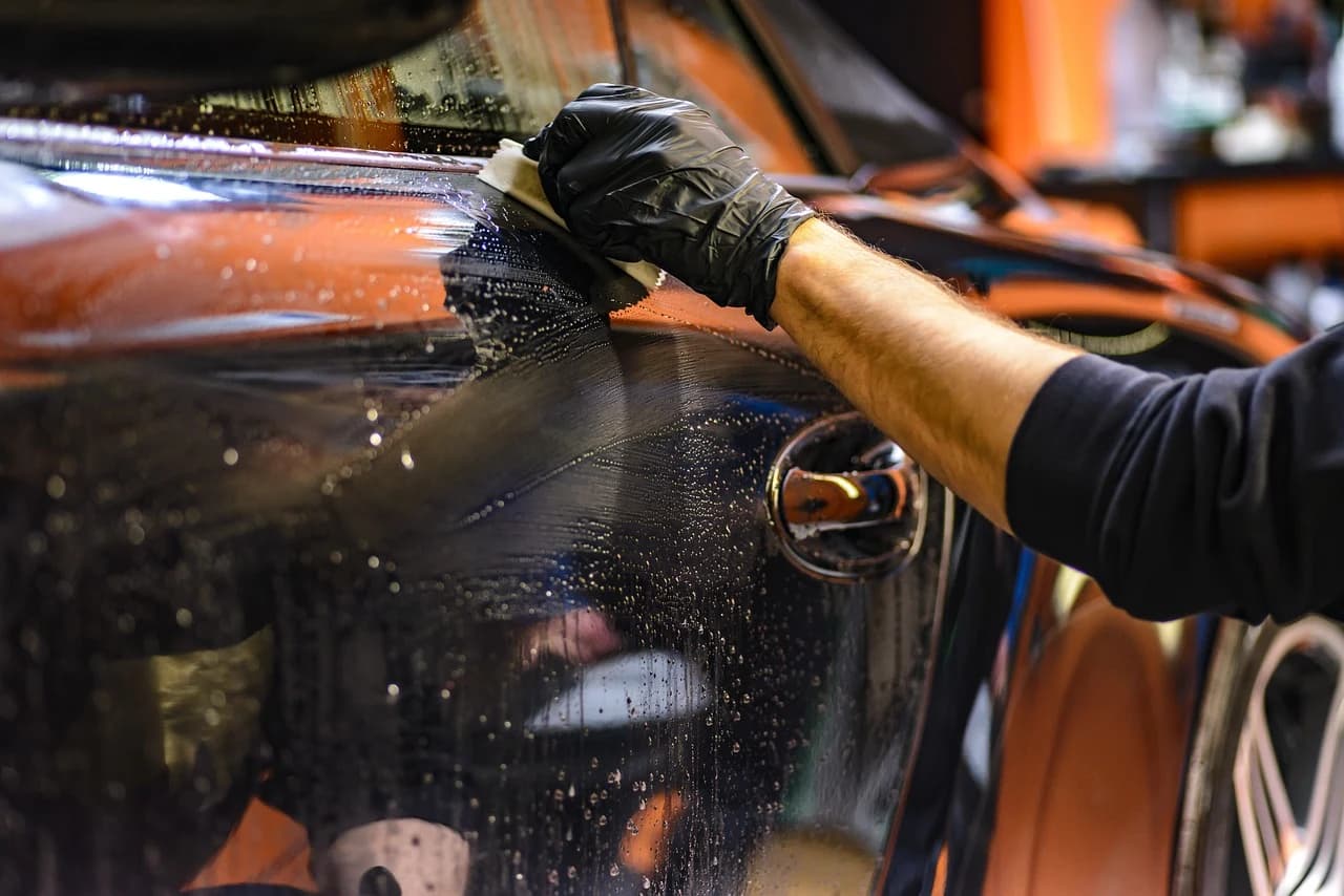 Detailer hand washing a black car with a sponge