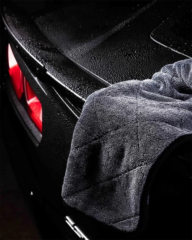 Water beading on black paint beside a microfiber towel